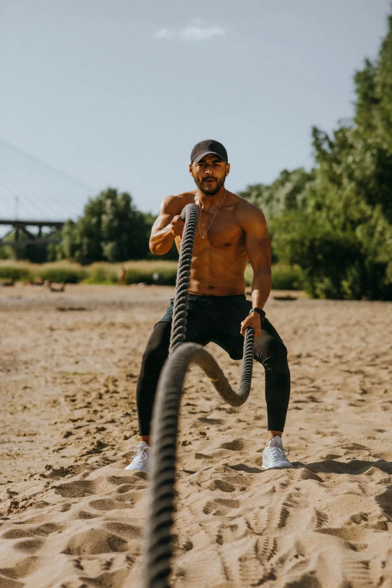 shirtless muscular man battle ropes beach