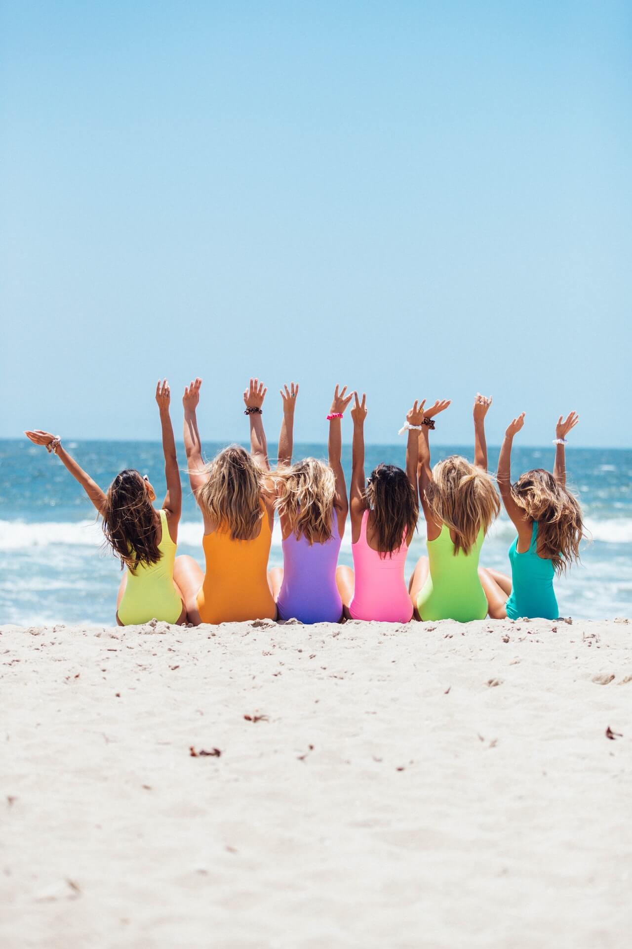 girls raising their hands at the beach