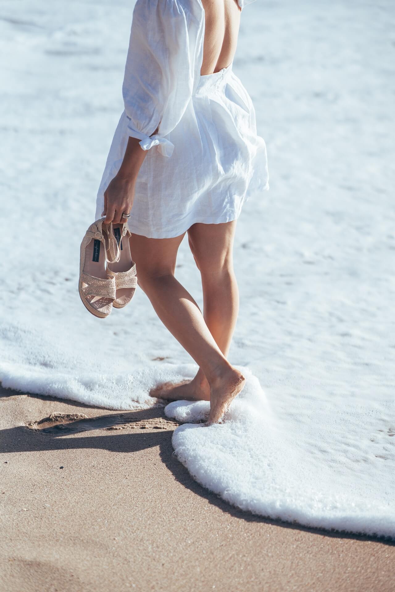 holding sandals in hand while walking along the shore